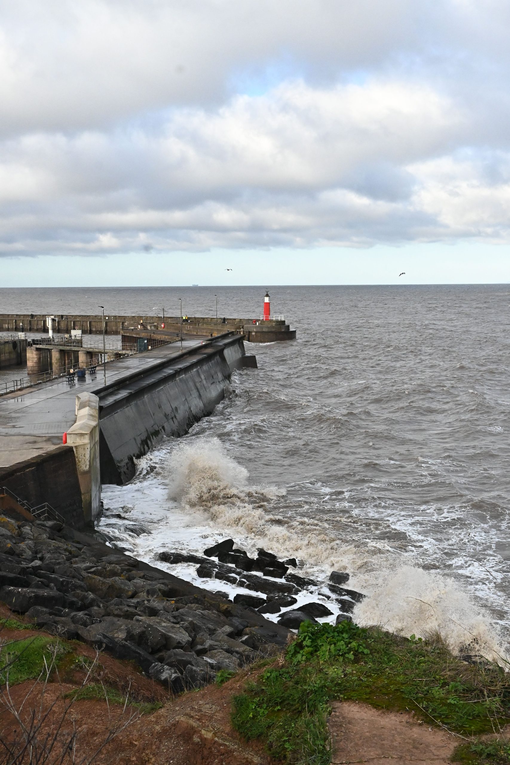 Waves beside Watchet Harbour wall and harbour light in Somerset