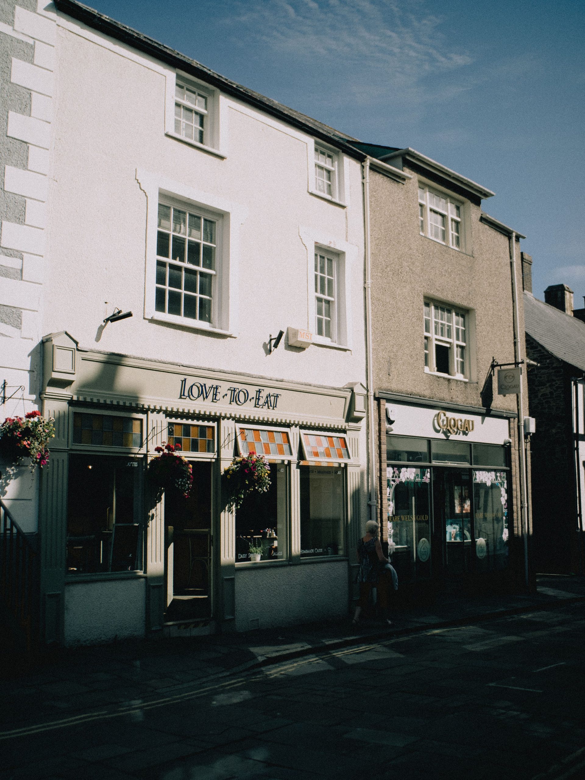 Traditional shops and café in Lostwithiel town centre, Cornwall, with historic buildings and hanging flower baskets.