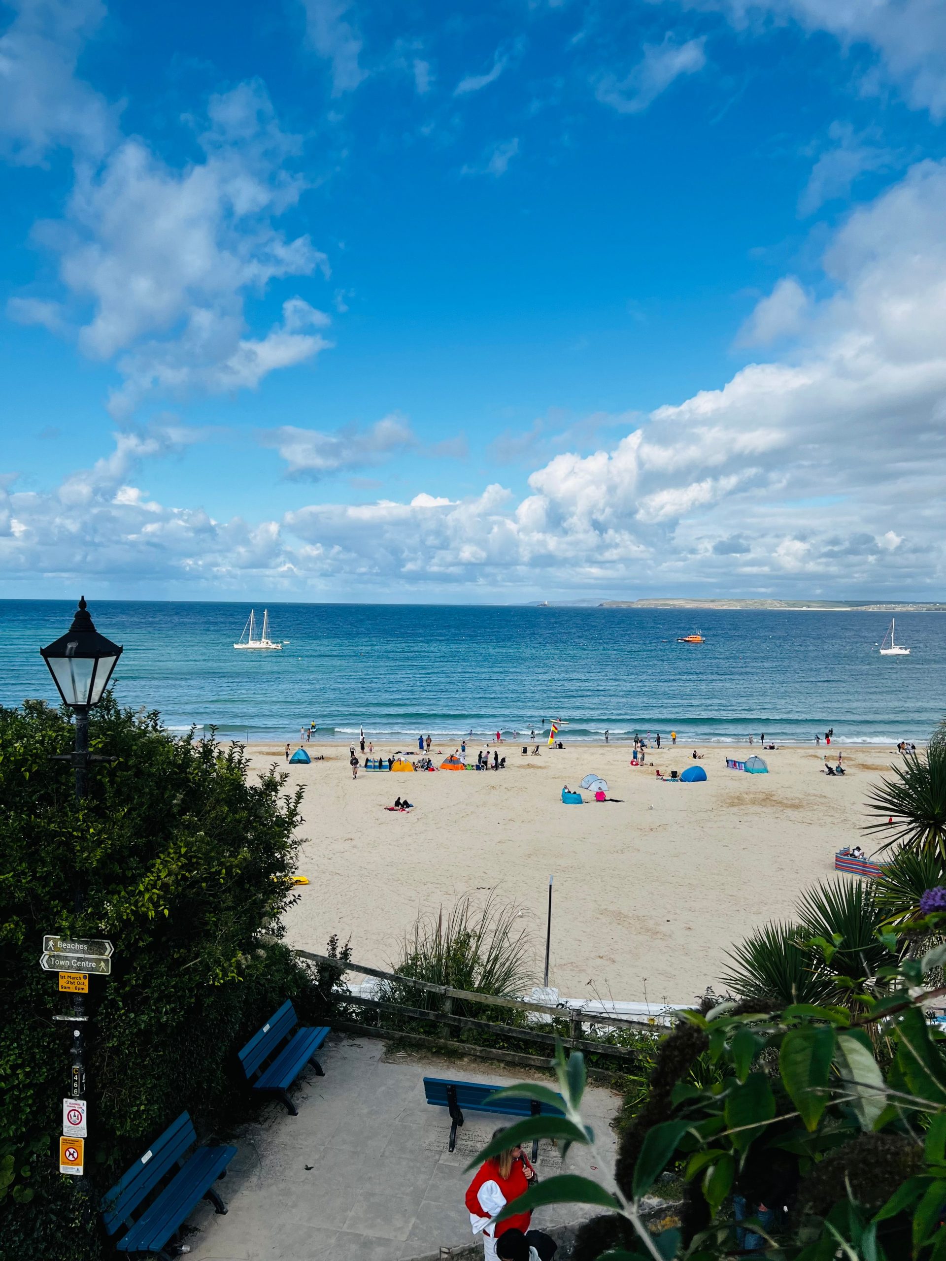 Sandy beach in Cornwall with sailing boats, blue sea and visitors enjoying the coastline near Penzance.