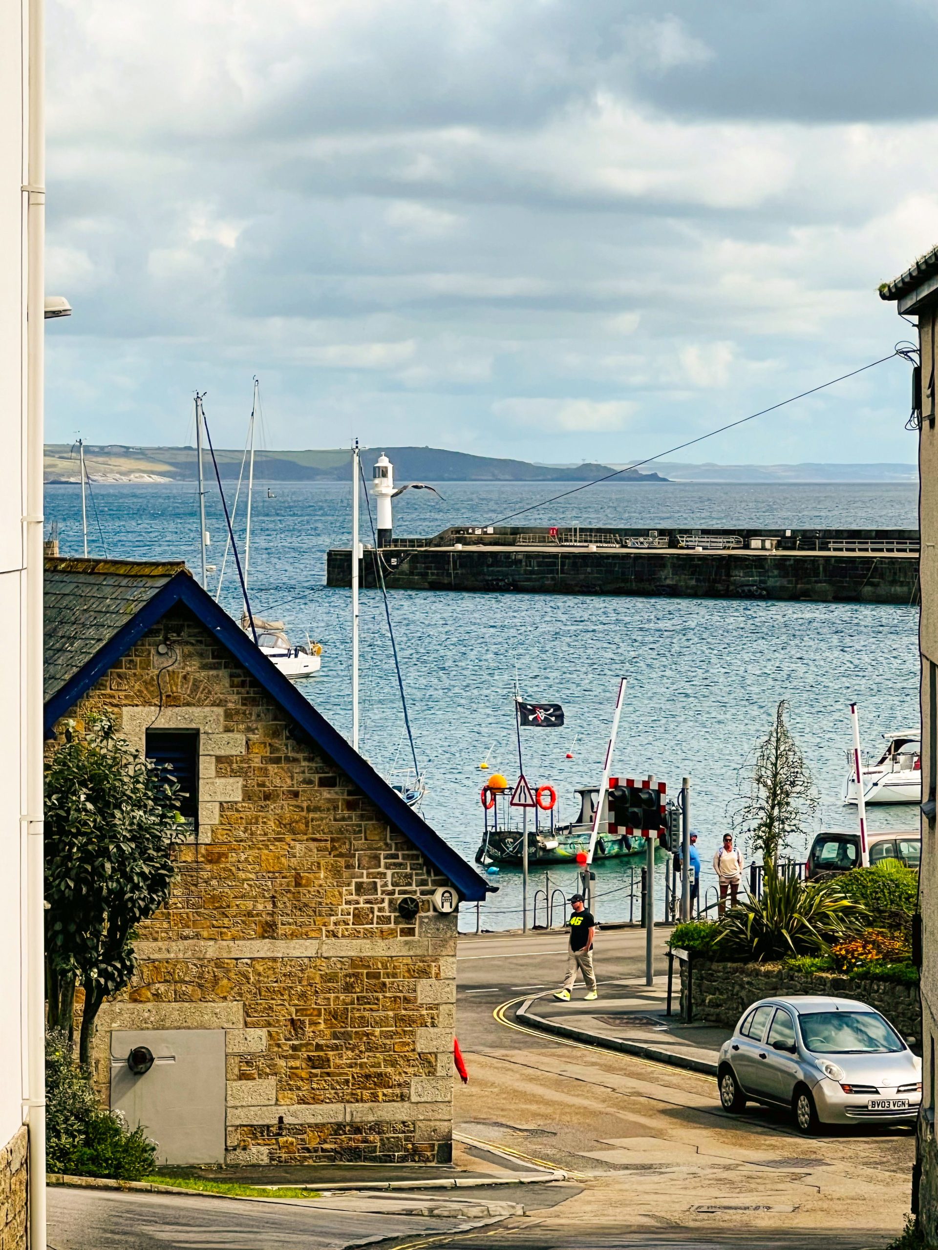 Penzance Harbour in Cornwall, showing the lighthouse, harbour wall, sailing boats and traditional stone buildings overlooking the sea.