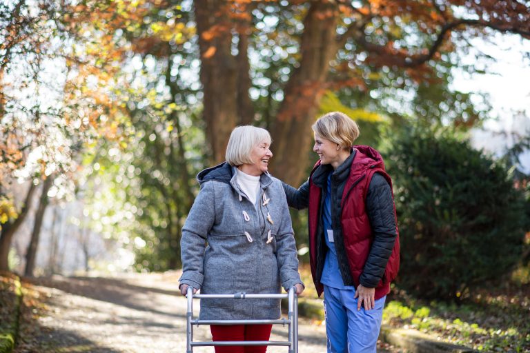 Older woman using a walking frame while enjoying an outdoor walk with a companionship carer as part of Companionship Care at Home