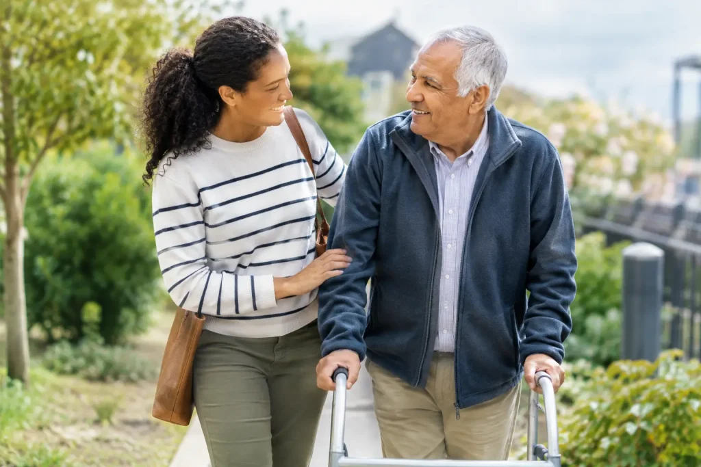 Older man using a walking frame beside a woman on an outdoor path