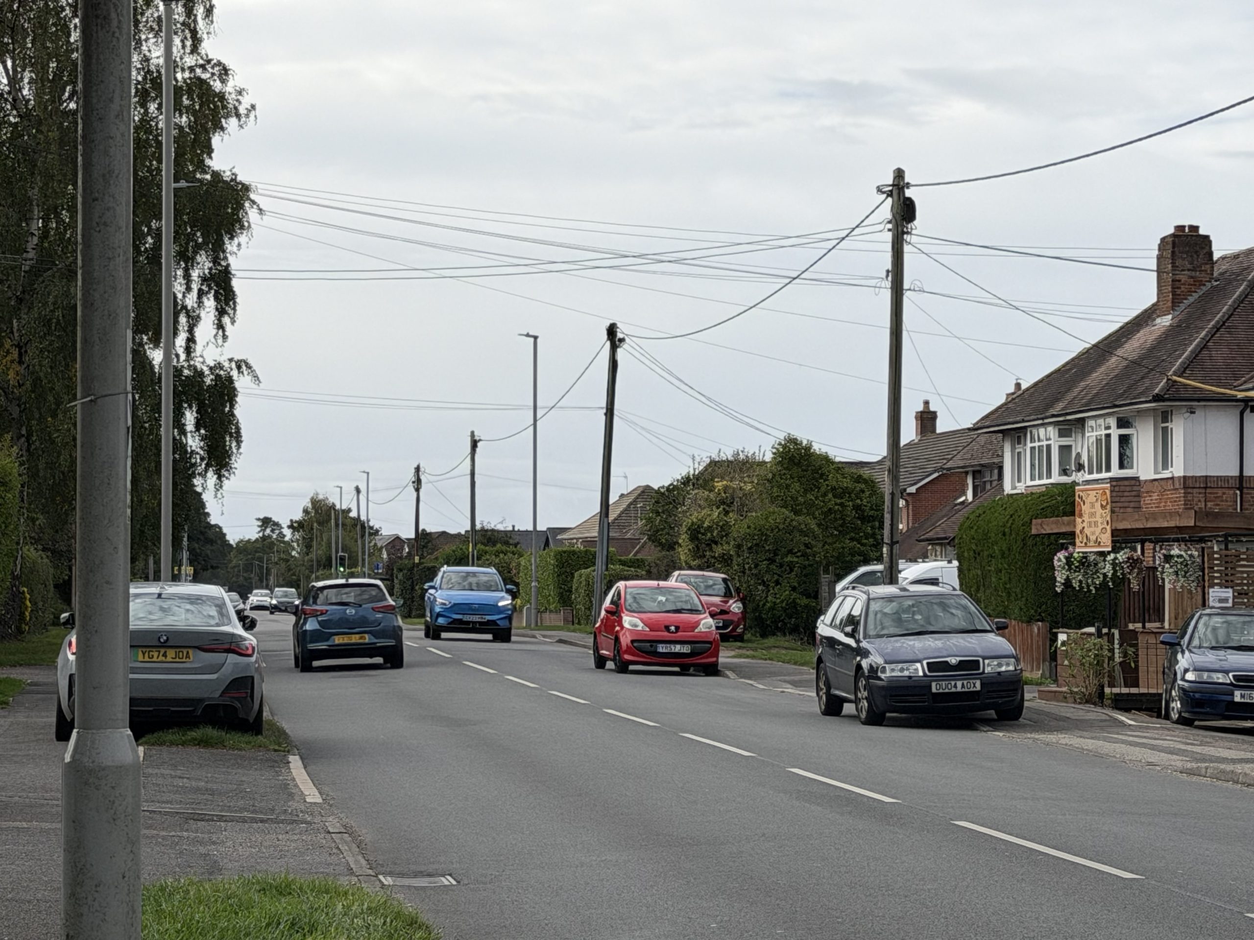 Residential street in Corfe Mullen, Dorset, with traditional houses, gardens and roadside trees.