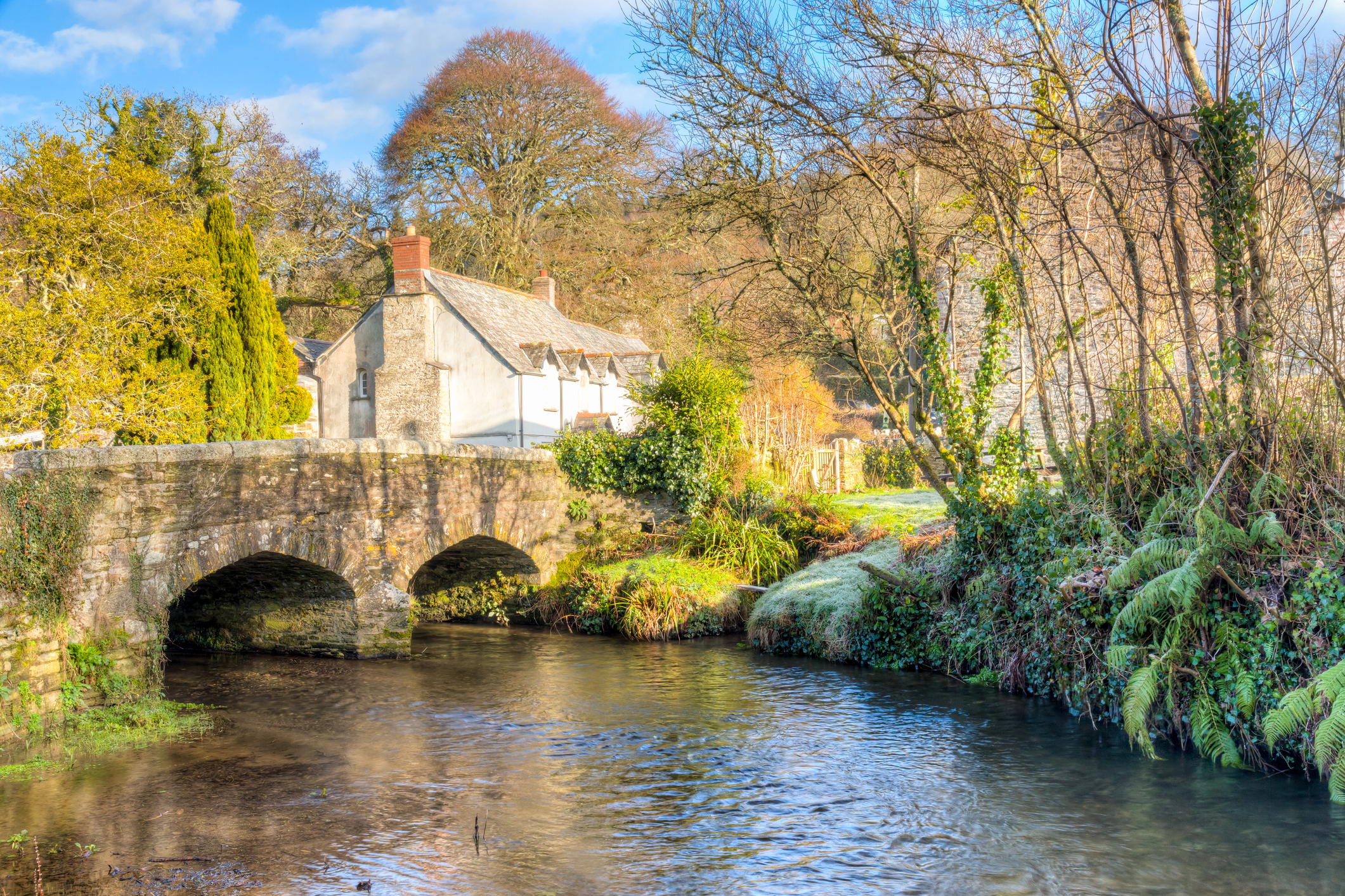 Historic stone bridge at Couch’s Mill near Lostwithiel, Cornwall, crossing a peaceful river beside a traditional cottage.