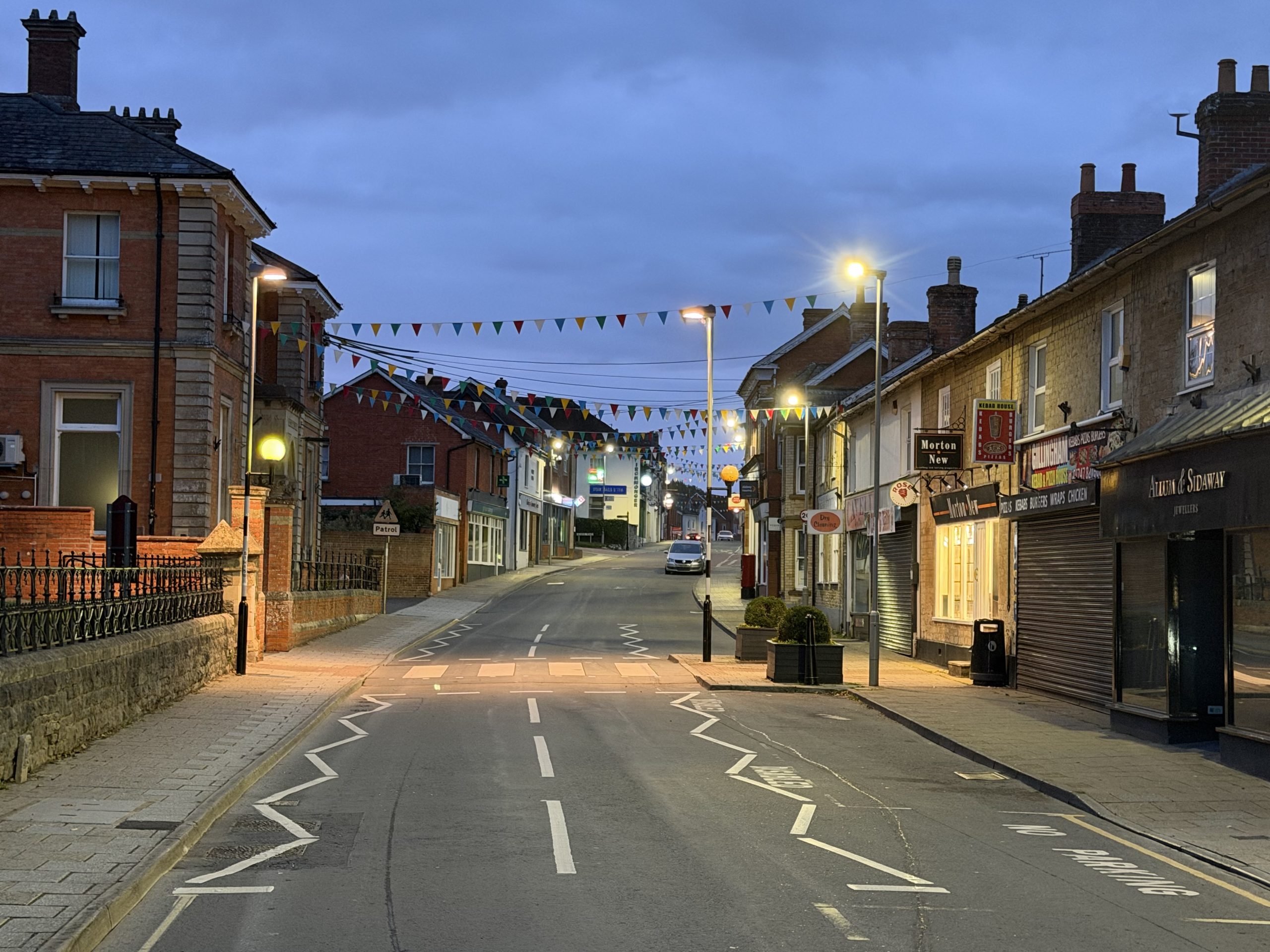 Gillingham High Street in Dorset with traditional shops, colourful bunting and street lighting at dusk.