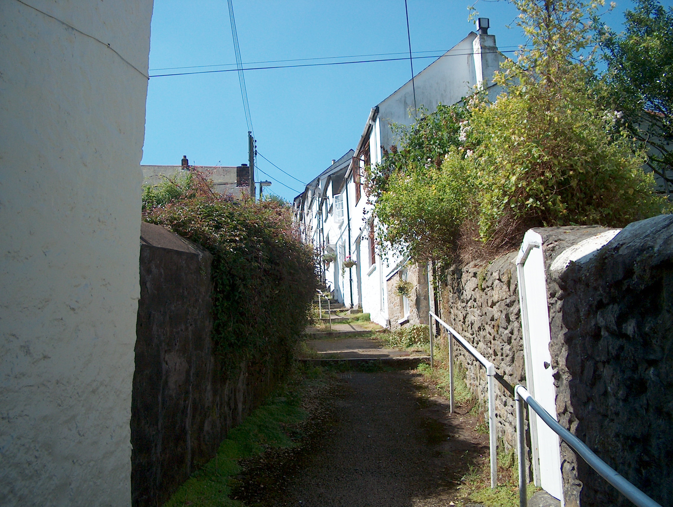Narrow historic mutton row in Penryn, Cornwall, with traditional whitewashed cottages, stone walls and steps.