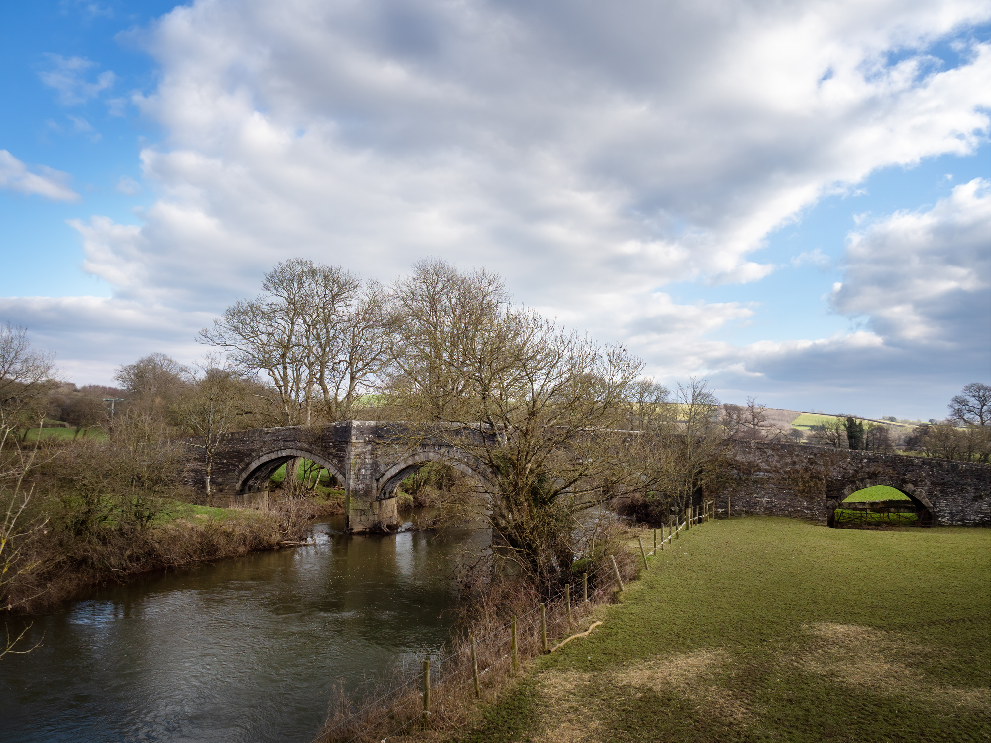 Historic stone arch bridge crossing a river surrounded by countryside