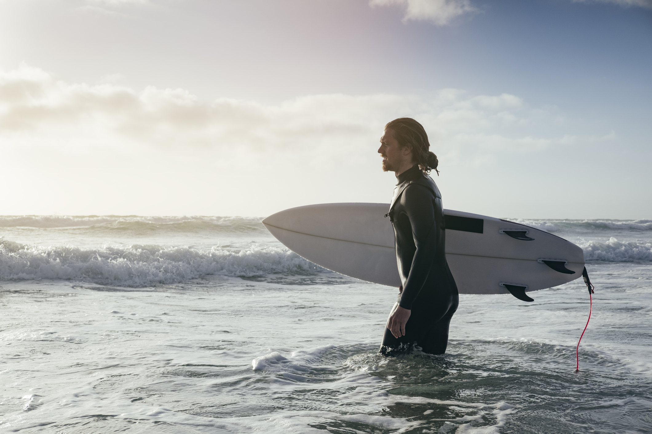 Surfer carrying a surfboard into the sea, representing the surfing lifestyle associated with Newquay, Cornwall.