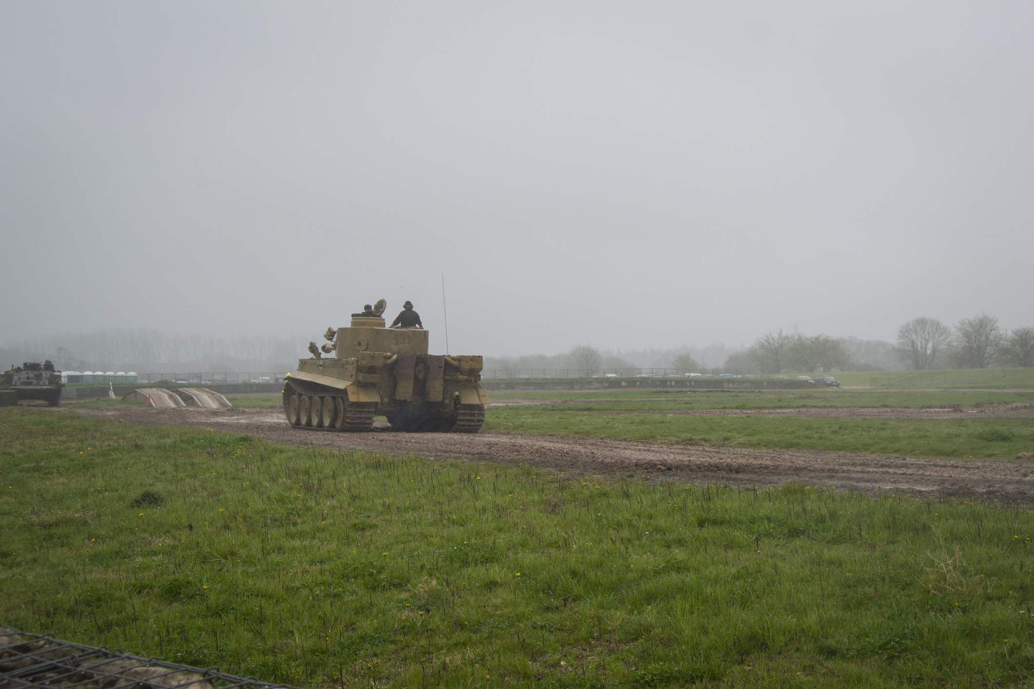 Historic Tiger tank driving across a grassy demonstration ground in misty weather at Bovington, Dorset.