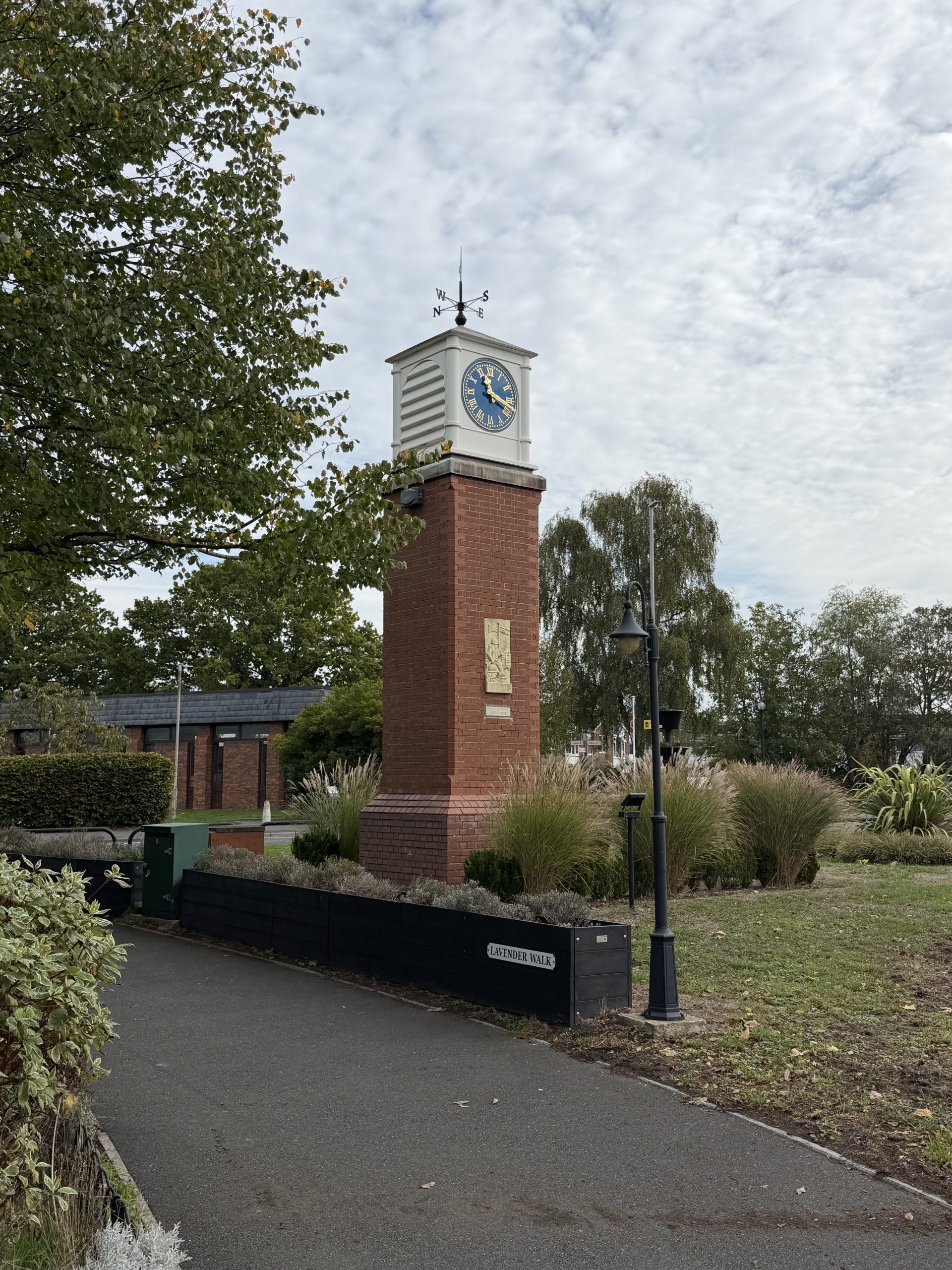 Brick clock tower at Lavender Walk in Upton, Dorset, surrounded by trees and landscaped planting.