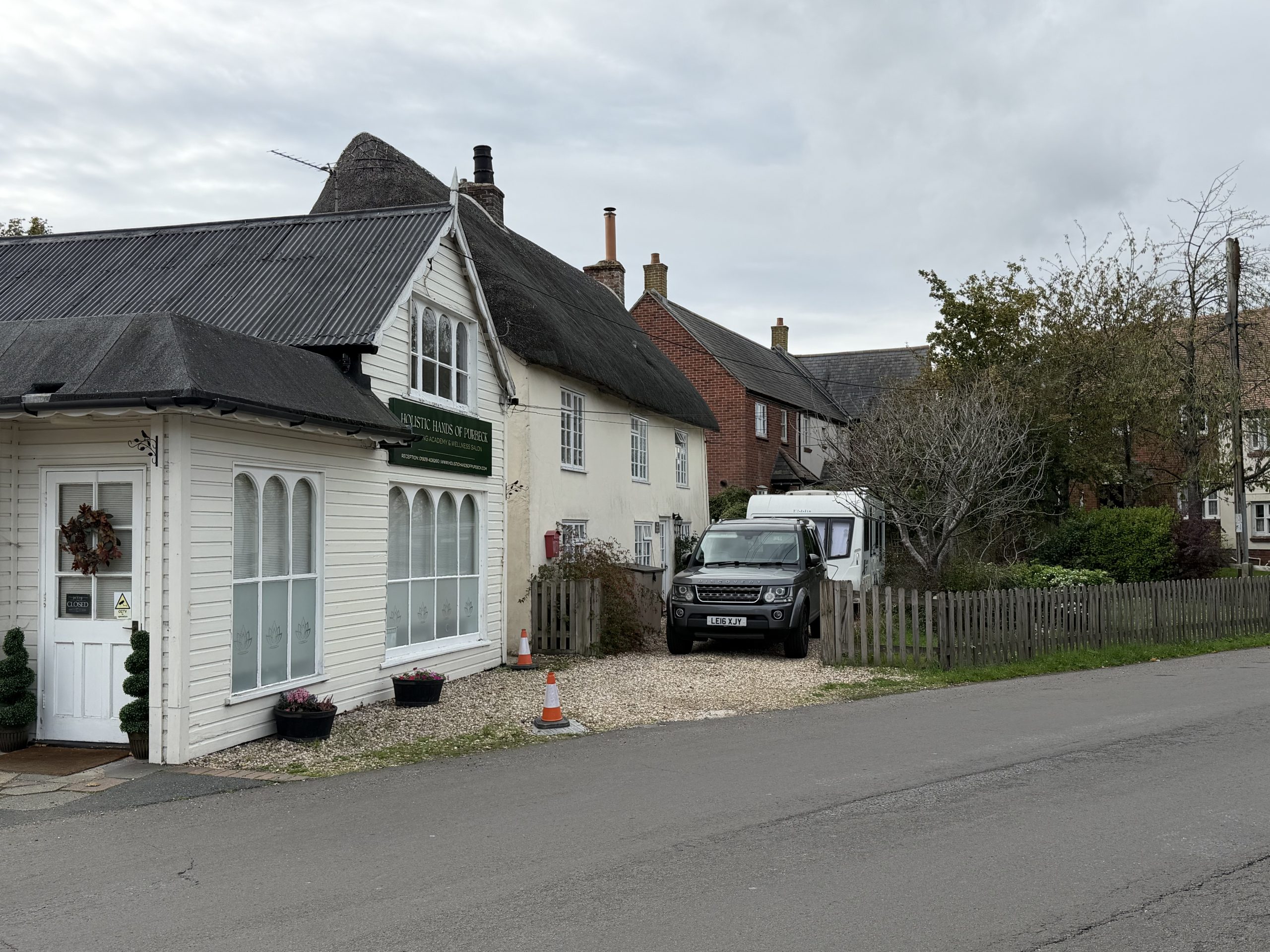 Traditional thatched cottages and village buildings along a residential street in Wool, Dorset.