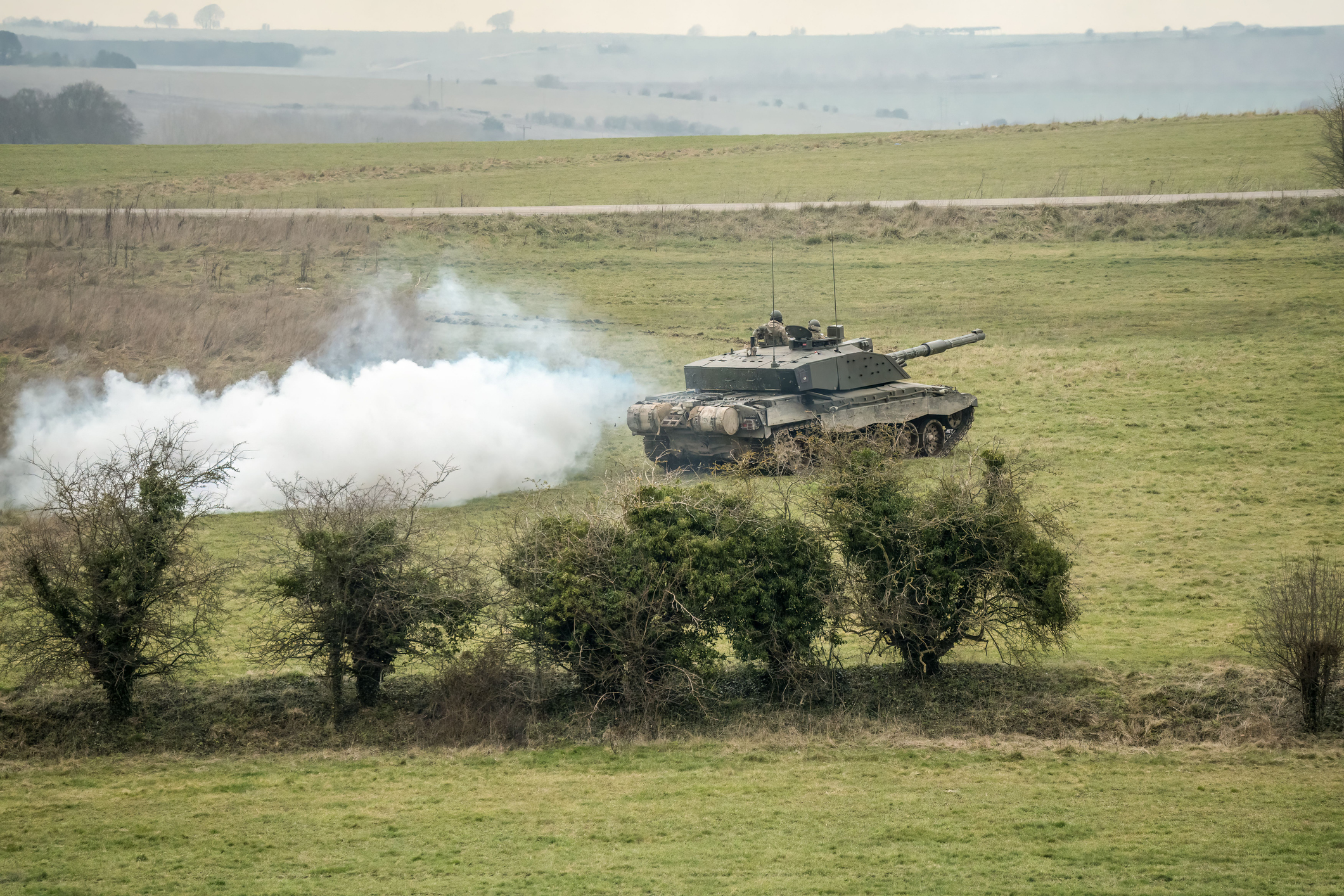 Military tank with white smoke on open grassy training grounds near Bovington in Dorset.
