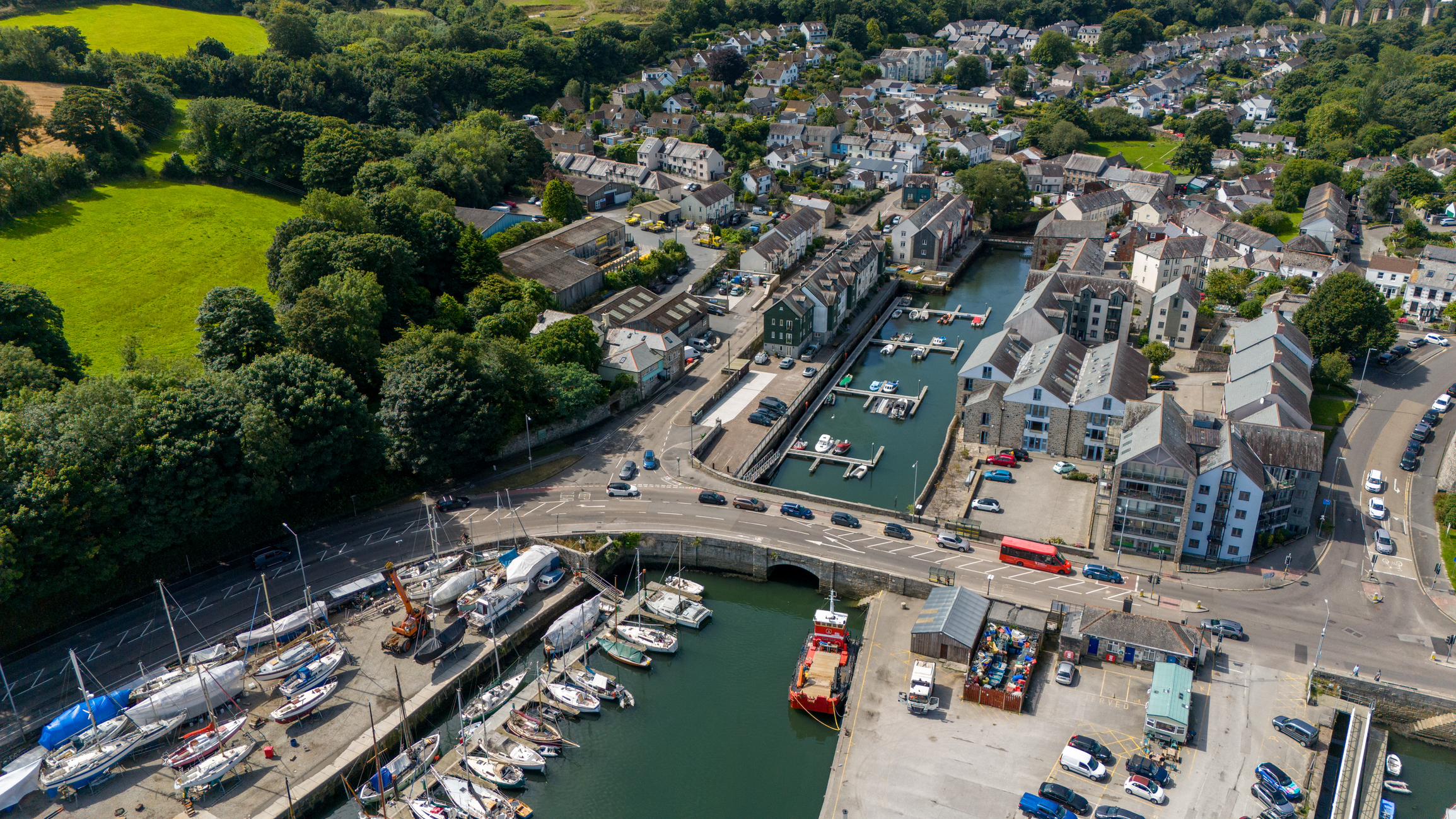 Aerial view of Penryn inner harbour in Cornwall, showing moored boats, waterfront buildings and surrounding residential streets.